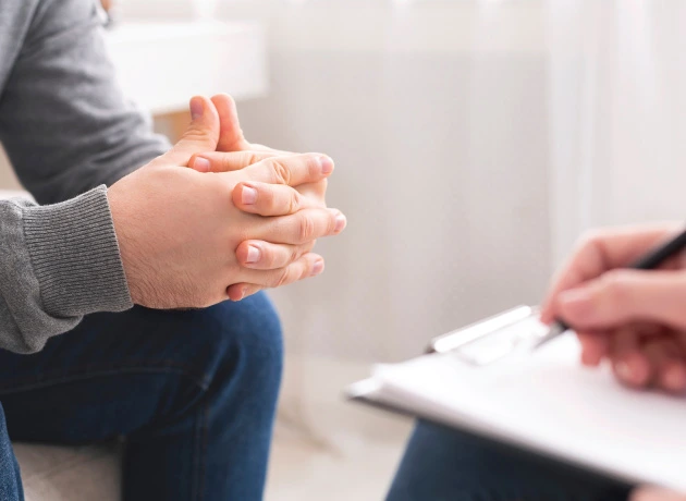 young adult male sitting with hands clasped together talking with attentive counselor taking notes